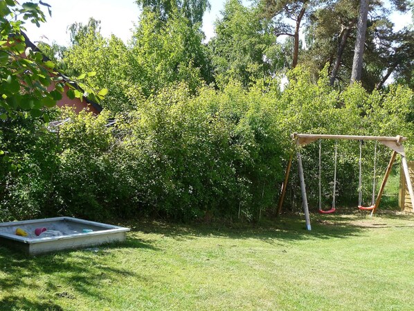 A backyard with a swing set, a sandbox, and dense foliage.