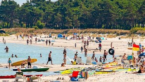 Uma praia cheia de pessoas, barcos e cadeiras de praia.
