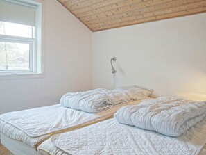 A bedroom with a wooden ceiling, a window, and a bed with two pillows.