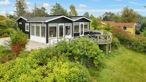 A small, single-story cabin with a deck and large windows, surrounded by lush greenery. - 7 Person Holiday Home in Knebel-by Traum (Knebel)