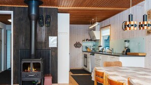 A cozy room with a wood-burning stove, a kitchen with modern appliances, and a dining area with wooden furniture. - 7 Person Holiday Home in Knebel-by Traum (Knebel)