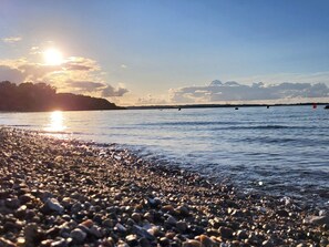 Uma praia de pedras com mar calmo e um pôr do sol ao fundo.