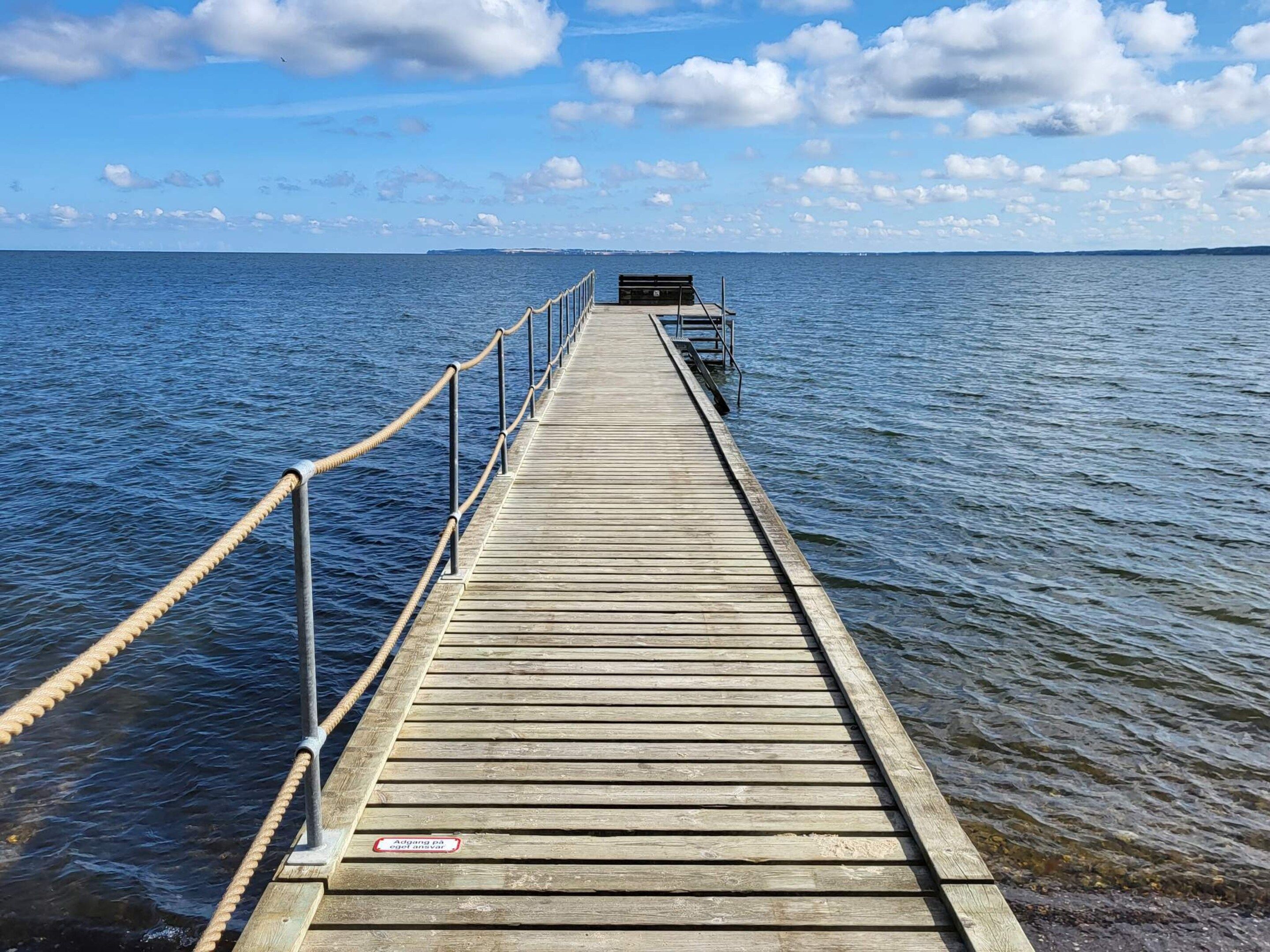 A wooden pier extending into calm water, with a metal railing on one side and a small structure at the end.