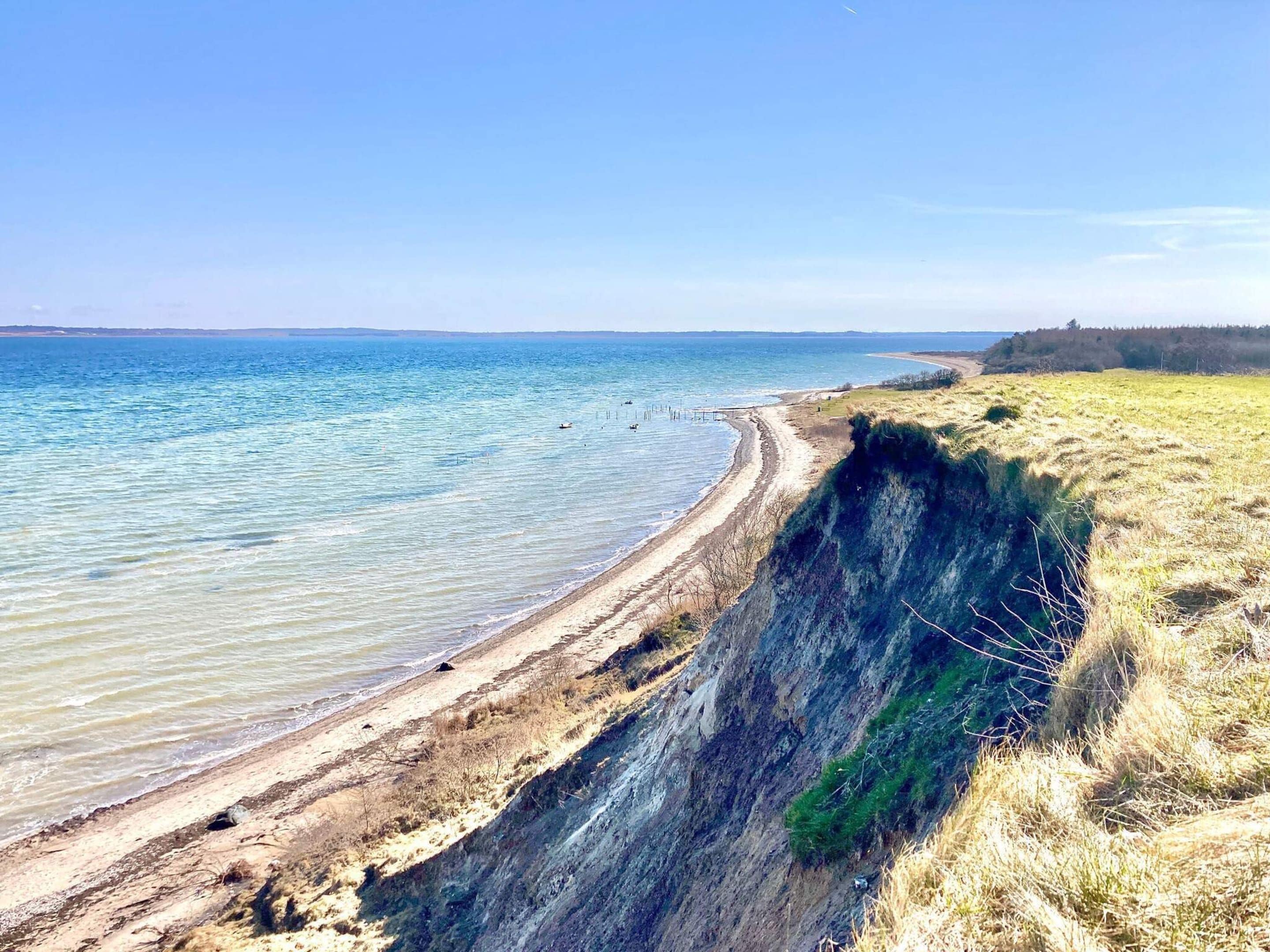 A coastal landscape with a steep cliff, a sandy beach, and a clear blue sky.