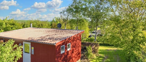 En rød bygning med et tegltag, en dør og vinduer, omgivet af grønt og en klar himmel.