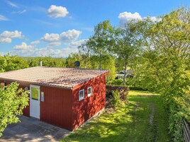 En rød bygning med et tegltag, en dør og vinduer, omgivet af grønt og en klar himmel.