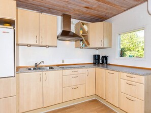 A kitchen with light wood cabinets, a stainless steel sink, a built-in stove, and a window with a view of greenery.