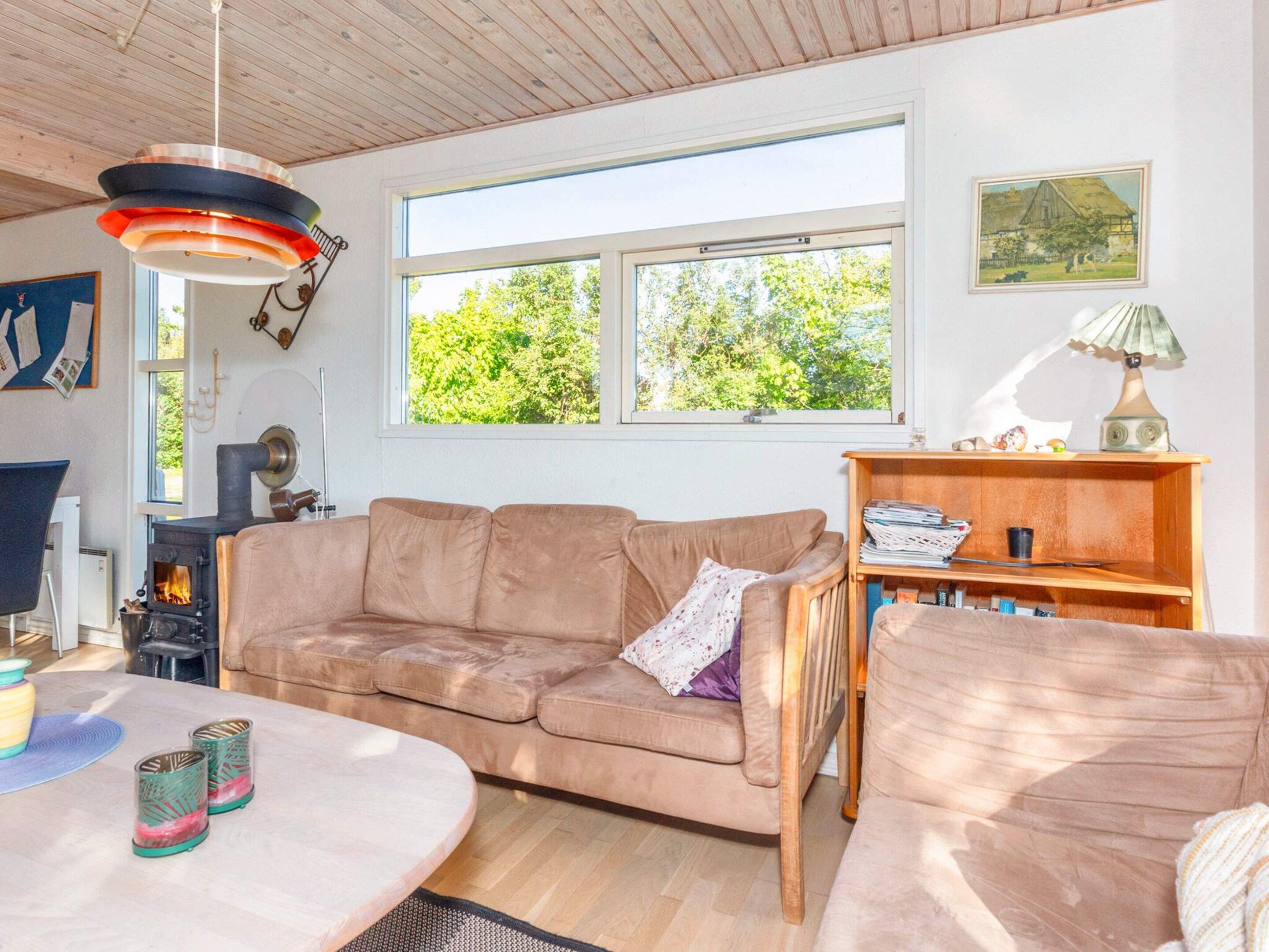 Una sala acogedora con un sofá color beige, una mesa de madera y un ventanal con vistas a árboles.