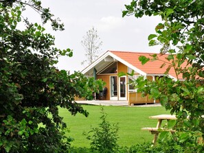 A wooden house with a red roof, a covered porch, and a grassy yard.