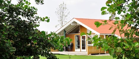 A single-story wooden house with a red roof, a covered porch, and a grassy yard.