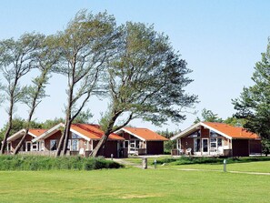 A row of cabins with red roofs, surrounded by trees and grassy areas.