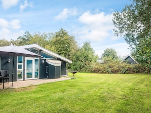 Une maison moderne dotée d’un patio, d’un espace extérieur aménagé et couvert, et d’une pelouse bien entretenue.