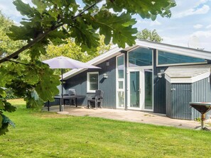 Une maison moderne dotée d’un patio, d’une table à manger avec des chaises et d’un grand parasol.