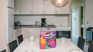 A modern kitchen with white cabinets, a coffee maker, and a box of TriViAl Pursuit GENUS-UDGAVE.