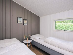 A room with two single beds, a small round table with a vase of flowers, and a window with a view of greenery.