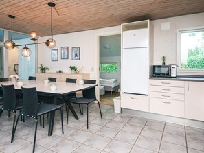 A modern kitchen with a dining area, featuring a wooden ceiling, a dining table with chairs, a built-in oven, and a window with a view of greenery. - 8 Person Holiday Home in Orsted (Ørsted)
