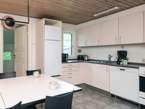 A modern kitchen with white cabinets, a dining table with chairs, a coffee maker, and a dishwasher.