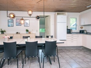A modern kitchen with a dining area, featuring a wooden ceiling, a white refrigerator, and a tiled floor.