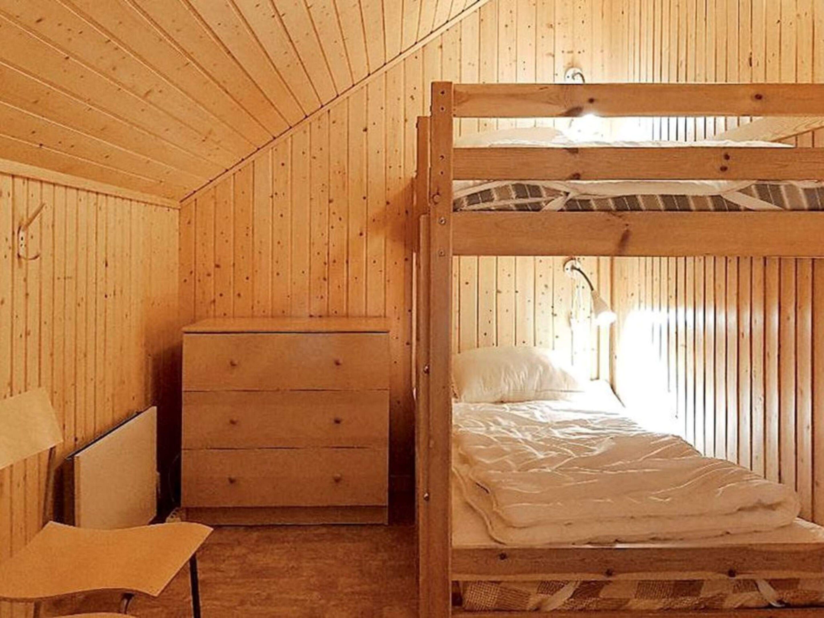 A bunk bed with a wooden headboard, a single drawer dresser, and a chair.