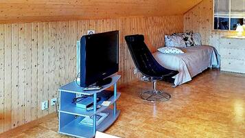A room with a television on a stand, a black chair, a bed with pillows, and a dresser.