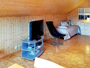 Een kamer met een televisie op een standaard, een zwarte stoel, een bed met kussens en een dressoir.