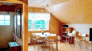 A room with a dining table, chairs, a bookshelf, and a window with a view of greenery. - 5 Person Holiday Home in Lammhult, Sverige (Lammhult)