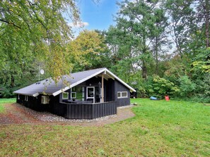A cabin with a porch, surrounded by trees and a grassy area.