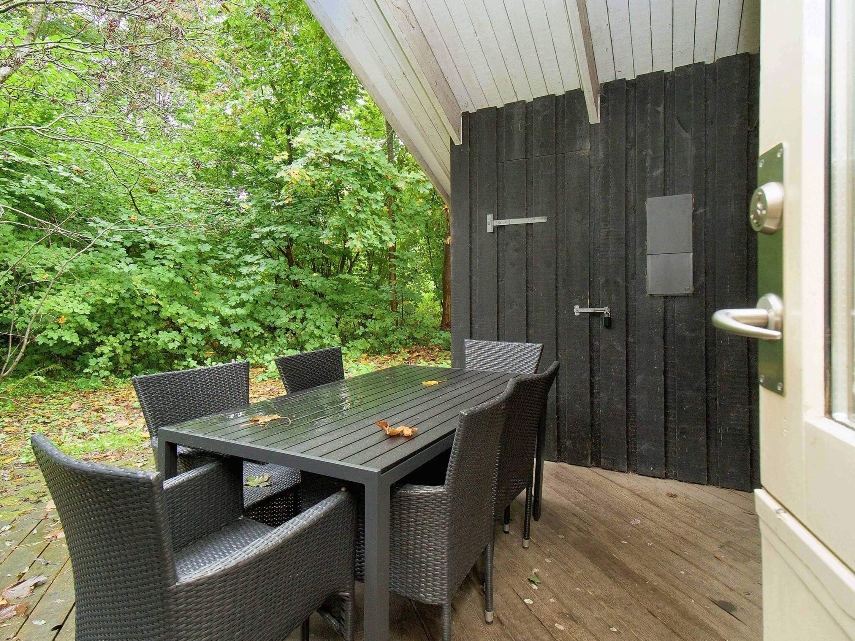 An outdoor dining area with a table and chairs, surrounded by a wooden deck and a black door.