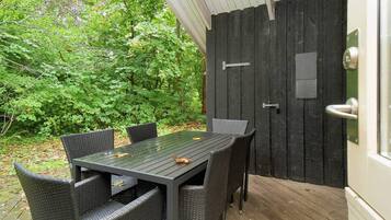 An outdoor dining area with a table and chairs, surrounded by a wooden deck and a black door.