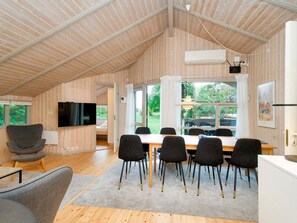 A spacious room with a high ceiling, a dining table with chairs, a television, and a window with curtains. - 8 Person Holiday Home in Melby (Melby)