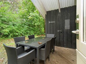 Un espacio de comedor al aire libre con una mesa y sillas, rodeado por una terraza de madera y una puerta negra.