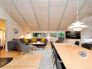 A modern living room with a wooden ceiling, a sofa set, a dining table, and a TV mounted on the wall. - 8 Person Holiday Home in Melby (Melby)