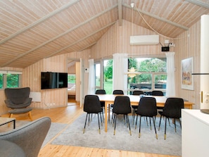 A spacious room with a high ceiling, a dining area with a table and chairs, a television mounted on the wall, and a window with a view of greenery outside. - 8 Person Holiday Home in Melby (Melby)