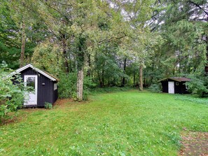 Eine abgelegene Hütte, umgeben von dichtem Wald, mit einer grünen Lichtung davor.