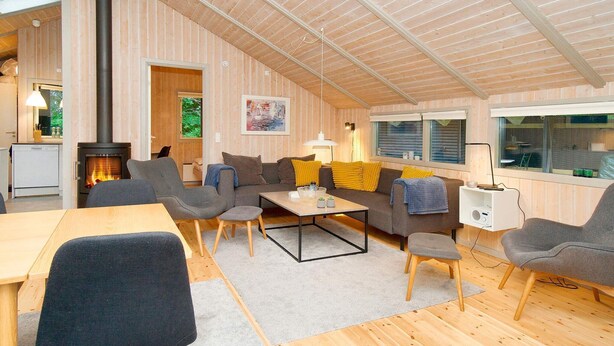 A cozy living room with a fireplace, wooden walls, and a dining area. - 8 Person Holiday Home in Melby (Melby)