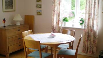 A dining area with a round table, four chairs, a wooden cabinet, and a window with floral curtains.