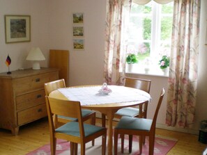 A dining area with a round table, four chairs, a wooden cabinet, and a window with floral curtains. - 4 Person Holiday Home in Gullspang (Gullspång)