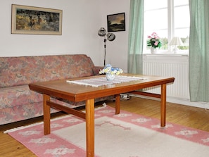 A living room with a wooden table, floral-patterned sofa, and a window with curtains. - 4 Person Holiday Home in Gullspang (Gullspång)