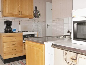 A kitchen with wooden cabinets, a coffee maker, a microwave, and a tiled backsplash. - 4 Person Holiday Home in Gullspang (Gullspång)