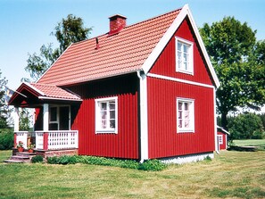 A red wooden house with a white porch and a chimney.
