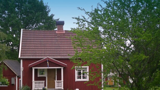 A red wooden house with a tiled roof, a porch with white railings, and a small lawn with a table and chairs. - 4 Person Holiday Home in Gullspang (Gullspång)