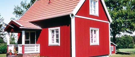 Ett rött trähus med ett sadeltak, en veranda och en skorsten.