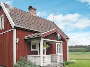 Une maison en bois rouge avec un porche blanc, une cheminée et un drapeau.