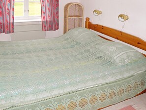 A bed with a patterned bedspread, a wicker chair, and a wall-mounted lamp. - 4 Person Holiday Home in Gullspang (Gullspång)