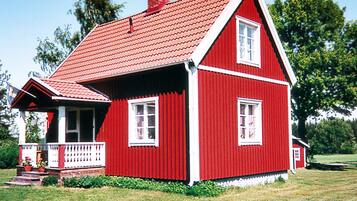A red wooden house with a gabled roof, a front porch, and a chimney.