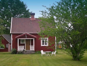 A red house with a tiled roof, a front porch with white railings, and a small table with chairs in the front yard.