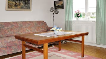 A living room with a wooden table, floral-patterned sofa, and a window with curtains.