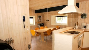 Une cuisine moderne dotée d’un îlot central, de murs en bois et d’un coin repas avec des chaises orange.