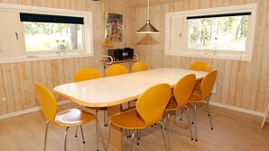 Un coin repas avec un mur lambrissé en bois, une table ronde et six chaises jaunes.