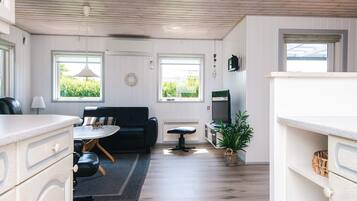 A modern living room with a black sofa, a dining table, a TV, and a potted plant.